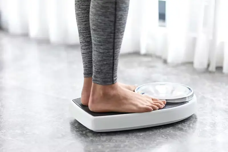 Person standing on a bathroom scale to check body weight and track weight loss progress
